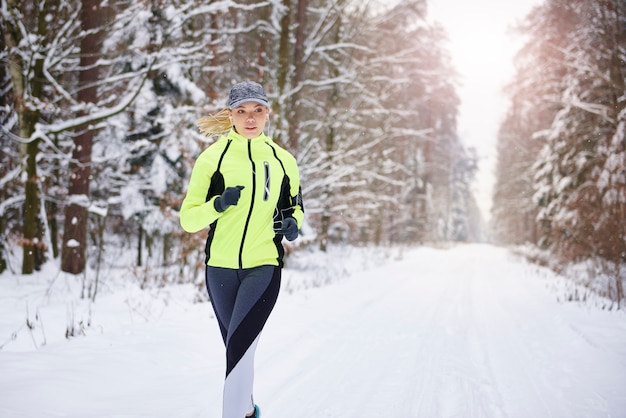Vista frontal de mulher correndo na floresta de inverno Foto gratuita