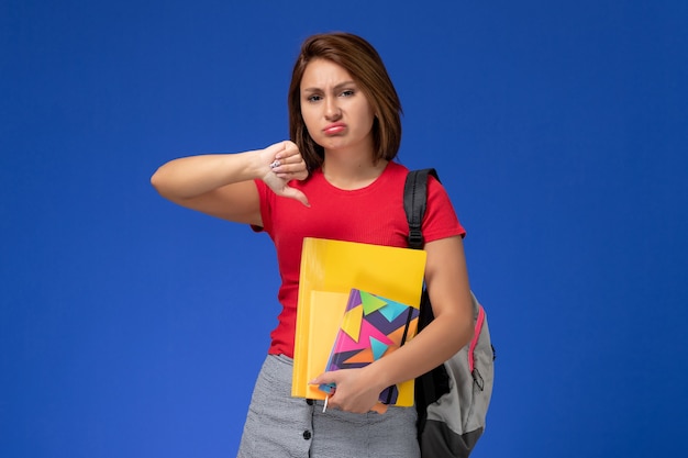 Vista Frontal Jovem Aluna De Camisa Vermelha Usando Mochila Segurando Arquivos E O Caderno 0564