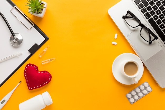 Vista superior da mesa de médicos com uma xícara de café; laptop contra fundo amarelo Foto gratuita