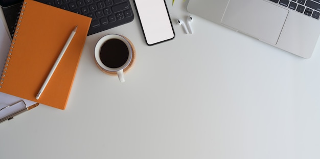 Vista superior do espaço de trabalho confortável com smartphone de tela em branco na mesa de madeira branca com material de escritório Foto Premium