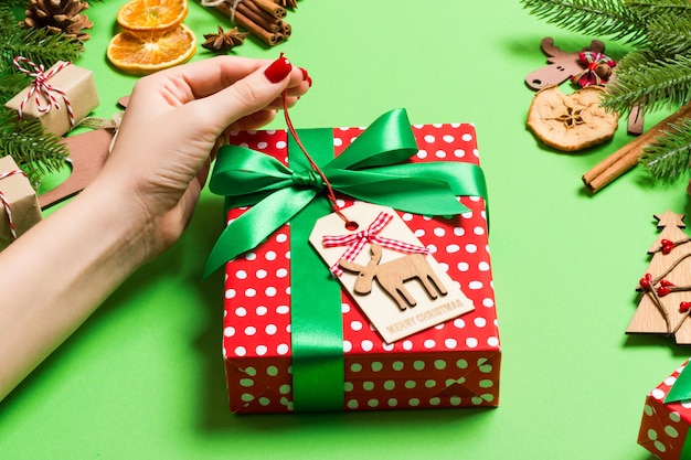 Vista superior mãos femininas segurando um presente de natal em verde festivo. árvore do abeto e decorações do feriado. feriado de ano novo Foto Premium