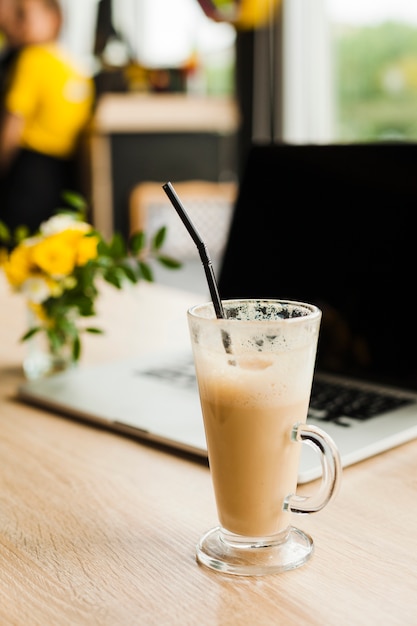 Xícara de café com leite com canudo na frente da desfocagem laptop na mesa Foto gratuita