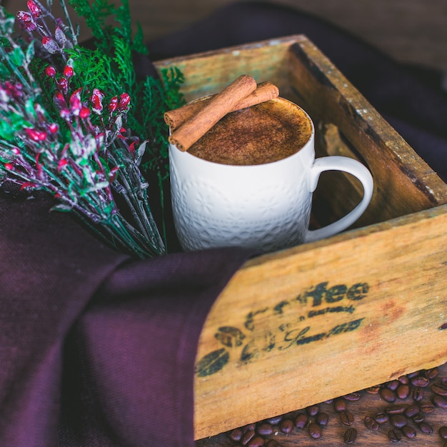 Xícara de café com leite, guarnecida com paus de canela, servida em caixa de madeira com galho de árvore Foto gratuita