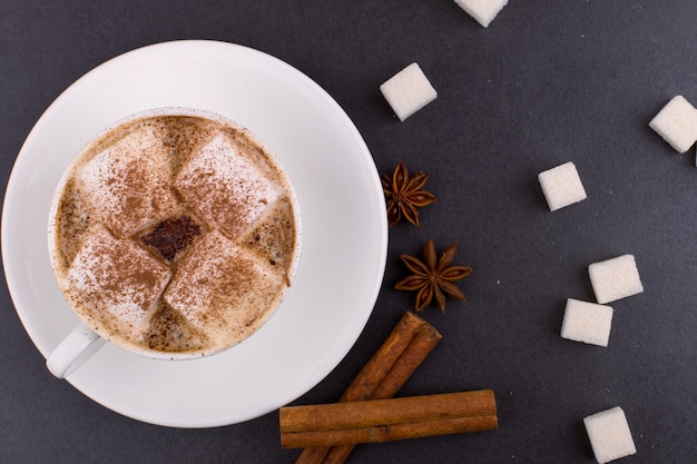 Xícara de café com marshmallows e cacau, açúcar, canela e anis estrelado, sobre um fundo cinza de pedra. Foto Premium