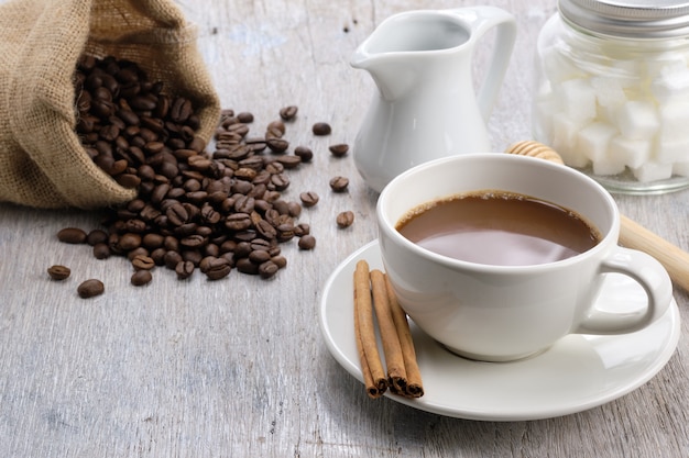 Xícara de café na mesa de madeira de manhã com feijão de café, açúcar cubo e canela. - imagem Foto Premium