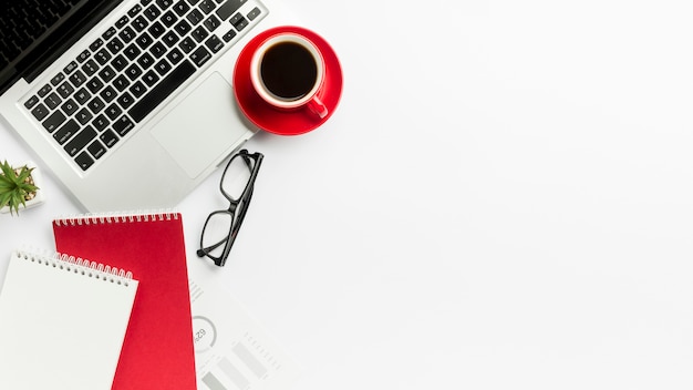 Xícara de café no laptop com óculos e bloco de notas em espiral no fundo branco Foto gratuita