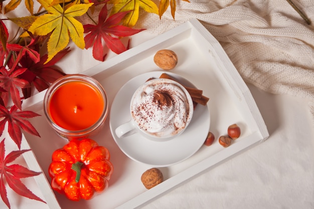 Xícara de chocolate quente e cremoso com espuma na bandeja branca com folhas de outono e abóboras no fundo Foto Premium