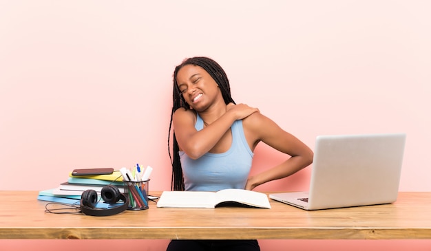 Afroamerikanerjugendlich-studentenmädchen mit dem langen umsponnenen haar an ihrem arbeitsplatz, der unter den schmerz in der schulter leidet Premium Fotos