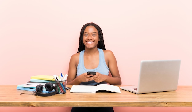 Afroamerikanerjugendlich-studentenmädchen mit dem langen umsponnenen haar an ihrem arbeitsplatz eine mitteilung mit dem mobile sendend Premium Fotos