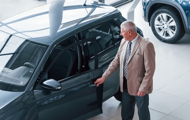 Alter mann in formeller kleidung, der im automobilsalon spaziert und