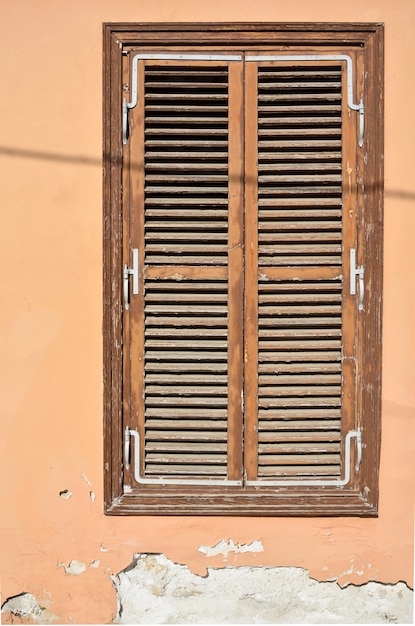 Altes braunes hölzernes fenster mit fensterläden und wand