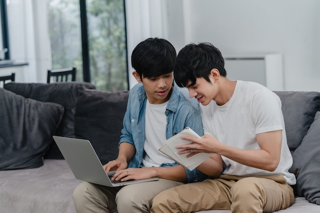 Arbeitslaptop der jungen asiatischen homosexuellen paare am modernen haus. die glücklichen männer asiens lgbtq + entspannen sich den spaß, der computer verwendet und zusammen ihre finanzen im internet analysiert, während lügensofa im wohnzimmer am haus. Kostenlose Fotos