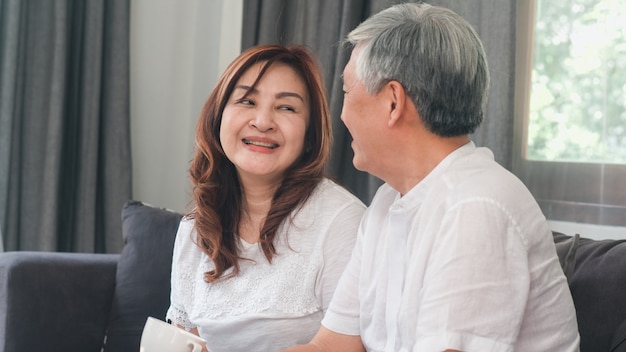 Asiatische ältere paare entspannen sich zu hause. asiatische ältere chinesische großeltern, glückliche lächelnumarmung des ehemanns und der frau, die zusammen beim auf sofa im konzept des wohnzimmers zu hause liegen spricht. Kostenlose Fotos