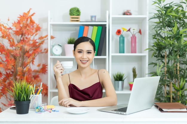 Asiatische geschäftsfrau machen eine kaffeepause, nachdem sie an der laptop-computer auf schreibtisch gearbeitet hat Kostenlose Fotos