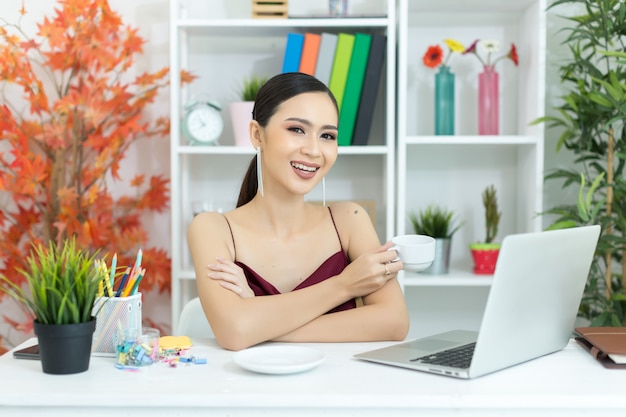 Asiatische geschäftsfrau machen eine kaffeepause, nachdem sie an der laptop-computer auf schreibtisch gearbeitet hat Kostenlose Fotos