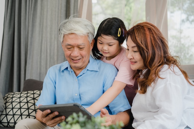 Asiatische großeltern und enkelin, die zu hause tablette verwendet. der ältere glückliche chinese, der großvater und die großmutter verbringen familienzeit mit dem jungen mädchen, das social media überprüft und liegen auf sofa im wohnzimmerkonzept Kostenlose Fotos