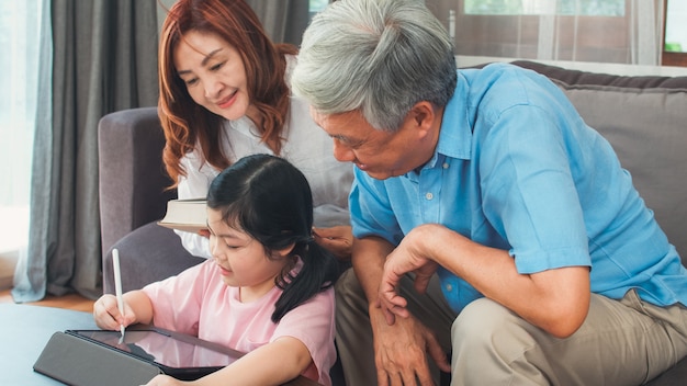 Asiatische großeltern und enkelin videoanruf zu hause. älterer chinese, großvater und großmutter glücklich mit dem mädchen, das den handyvideoanruf spricht mit dem vati und mutter zu hause liegt im wohnzimmer verwendet. Kostenlose Fotos