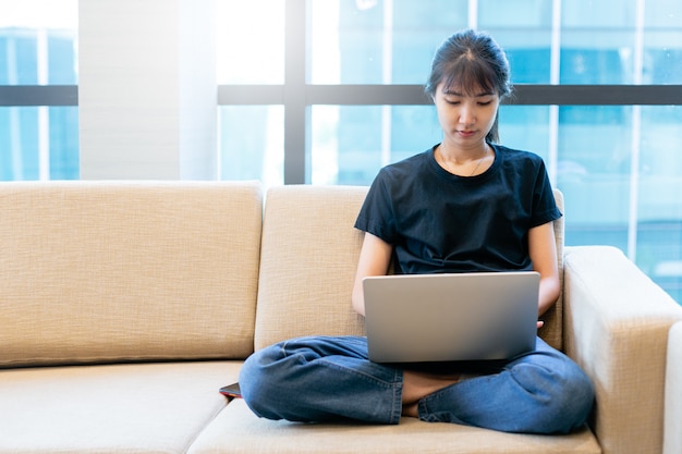 Asiatische junge frau, die mit laptop von zu hause aus