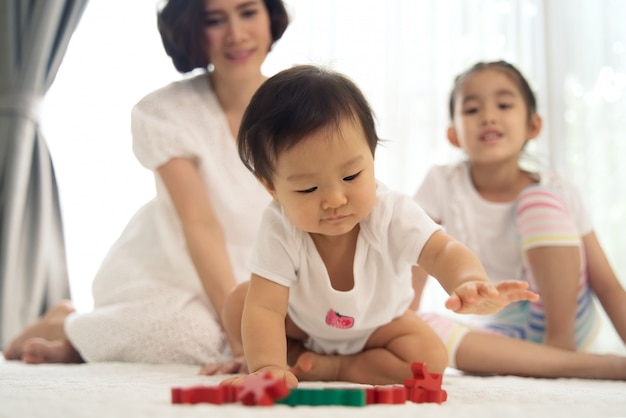 Asiatisches junges baby, das zu hause hölzerne spielwaren mit unterstützung von ihrer schwester und von mutter spielt. Premium Fotos