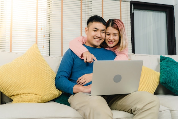 Attraktive asiatische süße paare unter verwendung des computers oder des laptops beim auf dem sofa liegen, wenn sie sich entspannen Kostenlose Fotos