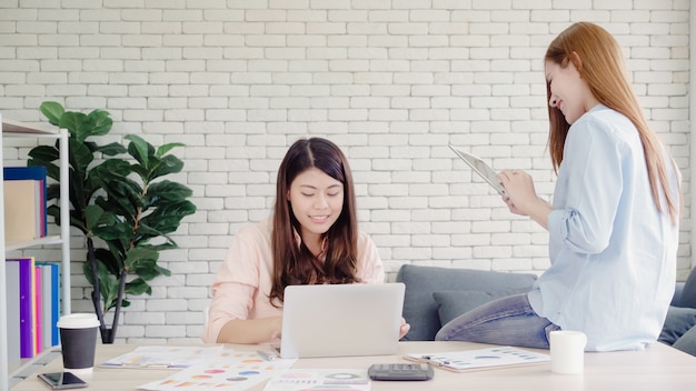 Attraktive intelligente kreative asiatische geschäftsfrauen in der intelligenten freizeitkleidung, die an laptop beim sitzen arbeitet Kostenlose Fotos
