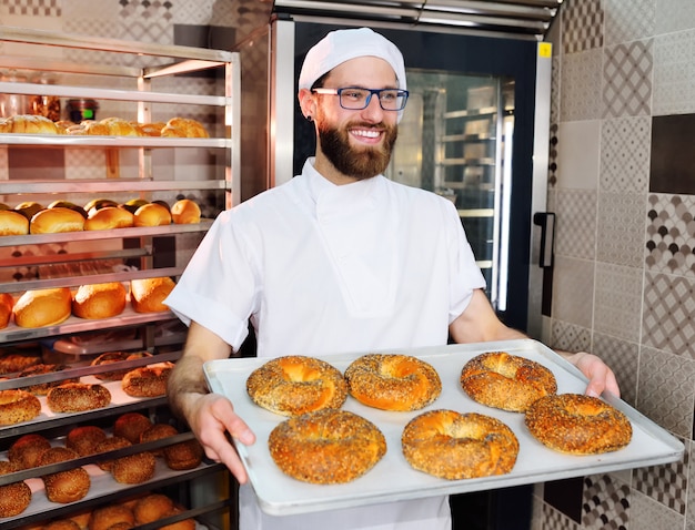 Attraktiver bäcker in der weißen uniform, die ein tellersegment mit frisch gebackenen bageln mit indischem sesam und mohn anhält Premium Fotos
