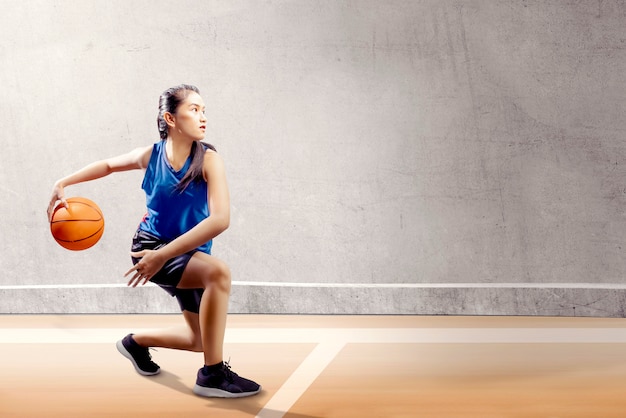 Attraktives asiatisches mädchen in der blauen sportuniform auf basketballzapfen verschiebt sich auf dem basketballplatz Premium Fotos