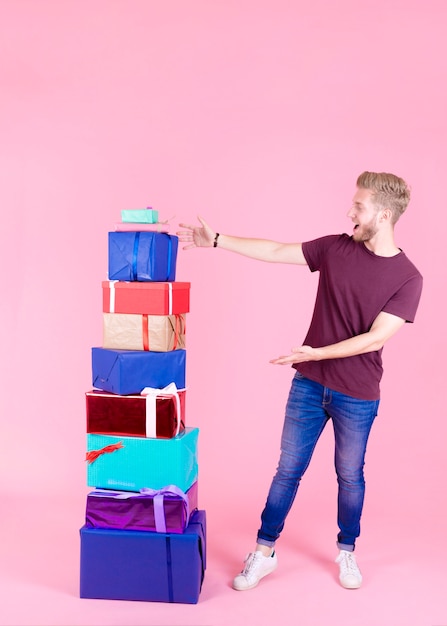 Aufgeregter Junger Mann Der Stapel Bunte Geschenke Gegen Rosa Hintergrund Zeigt Kostenlose Foto