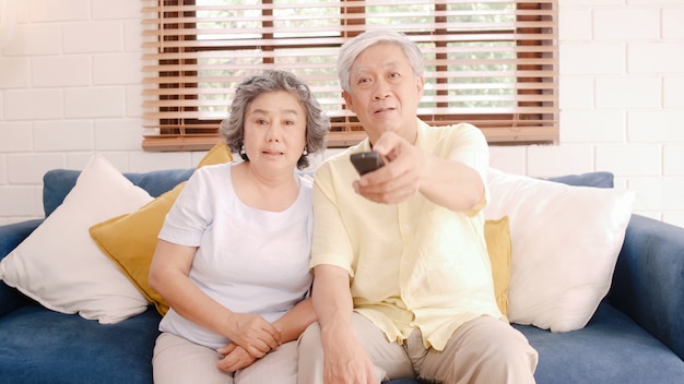 Aufpassendes fernsehen der asiatischen älteren paare im wohnzimmer zu hause, süße paare genießen liebesmoment beim auf dem sofa liegen, wenn sie zu hause entspannt werden. Kostenlose Fotos