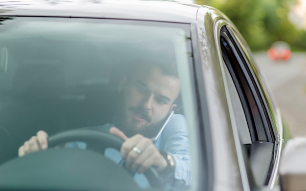 Bemannen sie das sitzen innerhalb des autos, das am handy gesehen durch windschutzscheibe spricht Kostenlose Fotos