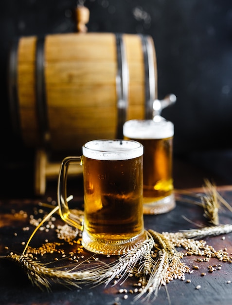 Biergläser und weizengewürz auf einer alten rustikalen hölzernen tabelle auf schwarzem hintergrund Premium Fotos