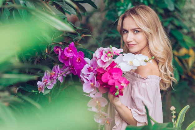 Blonde junge frau, die im garten hält orchidee steht Kostenlose Fotos