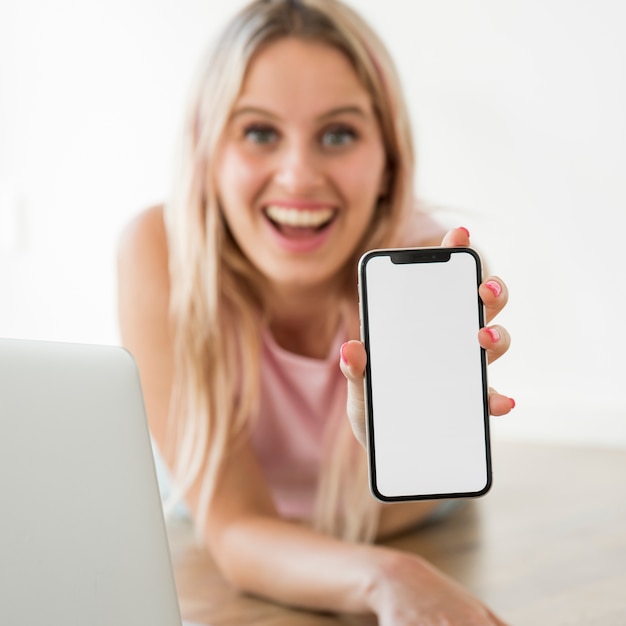 Blonder influencer, der smartphone auf dem boden zeigt Kostenlose Fotos