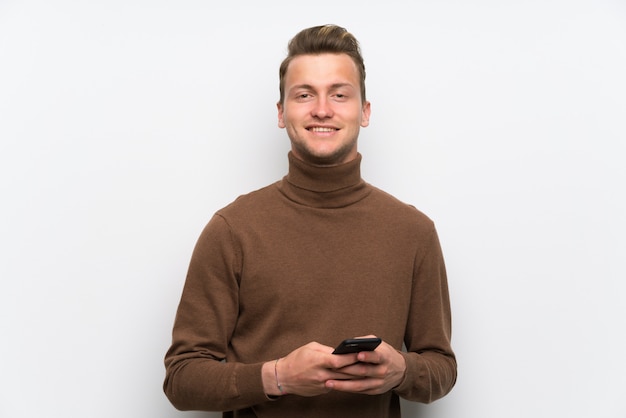 Blonder mann über der lokalisierten weißen wand, die eine mitteilung mit dem mobile sendet Premium Fotos