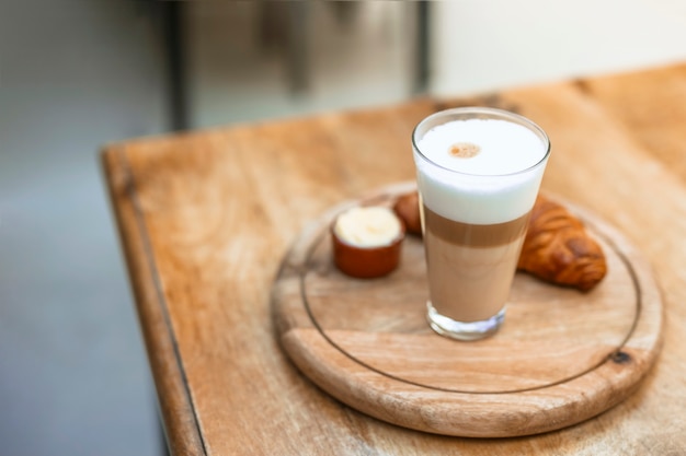 Cappuccino im glas mit hörnchen auf hölzernem rundem