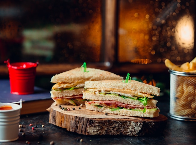 Club sandwich mit schinken, salat, tomate, käse und pommes frites auf holzbrett Kostenlose Fotos