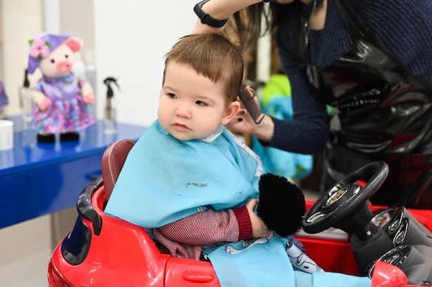 Das Kind Bekommt Beim Friseur In Einem Roten Auto Einen Haarschnitt Der Erste Haarschnitt Des Kindes Im Friseur Kleinkind Kind Bekommen Haarschnitt Premium Foto