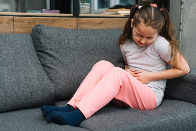 Das kranke mädchen, das auf grauem sofa sitzt, leidet unter magenschmerzen zu hause Kostenlose Fotos