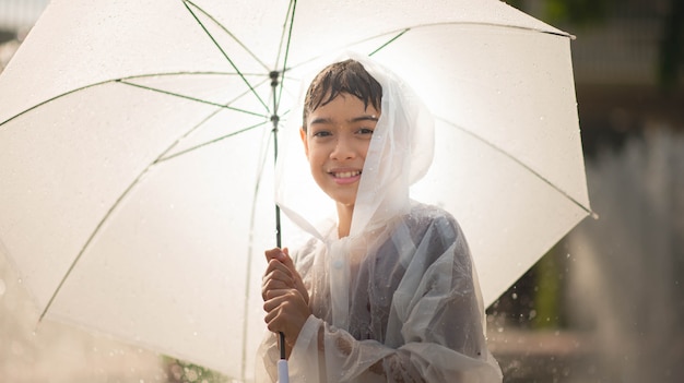 Der kleine junge, der wasser spielt, lässt brunnen unter dem stoff und dem regenschirm fallen Premium Fotos