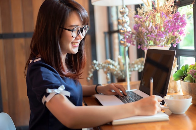 Die asiatische geschäftsfrau, die mit arbeitet, machen eine anmerkung mit einem notizbuch und einem laptop Premium Fotos