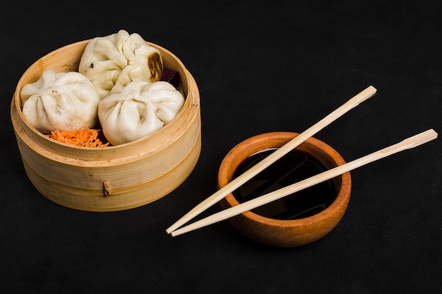 Dim sum zusammen mit dem karottensalat diente im kleinen dampferkorb und in der sojasoßenschüssel mit essstäbchen auf schwarzem hintergrund Kostenlose Fotos