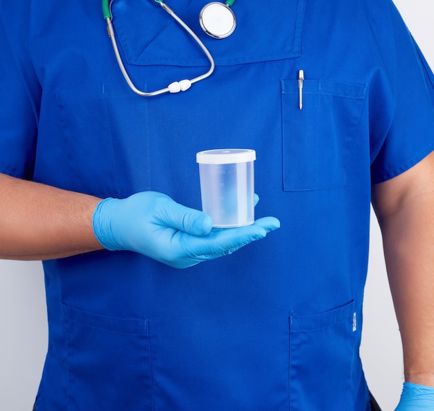 Doktor in der blauen uniform und in den latexhandschuhen hält einen leeren plastikbehälter für das entnehmen von urinproben Premium Fotos