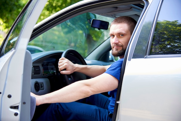 Ein bärtiger junger mann sitzt in einem auto mit einer offenen tür. Premium Fotos