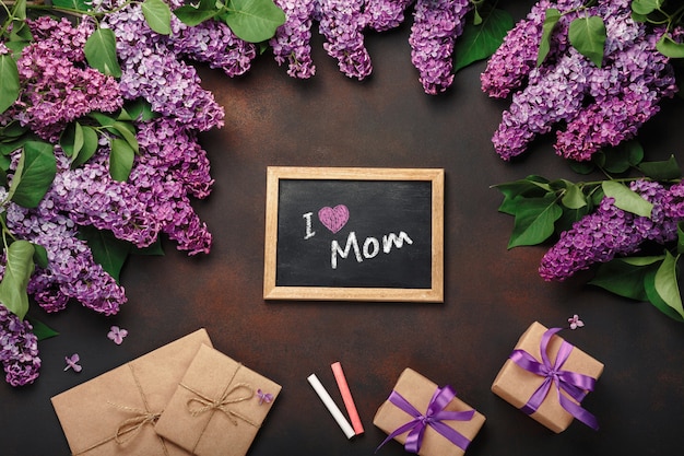 Ein blumenstrauß von fliedern mit kreidebrett, geschenkbox, handwerksumschlag auf rostigem hintergrund. muttertag Premium Fotos