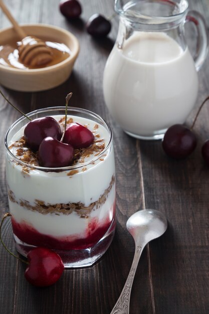 Ein glas kirschjoghurt mit müsli, honig und einem glas milch | Premium-Foto