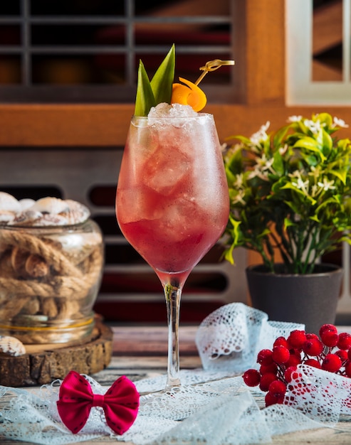 Ein glas rotes cocktail mit eiswürfeln und grünblättern