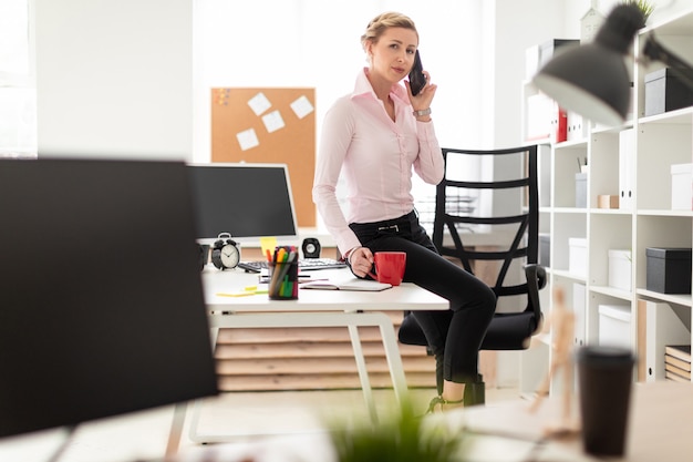 Ein Junges Blondes Mädchen Sitzt Auf Einem Tisch Im Büro Hält Eine Rote Tasse In Der Hand Und 