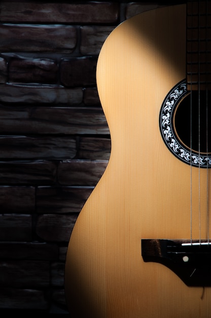 Ein lichtstrahl fällt auf eine akustikgitarre, die auf dem hintergrund einer backsteinmauer steht. Premium Fotos