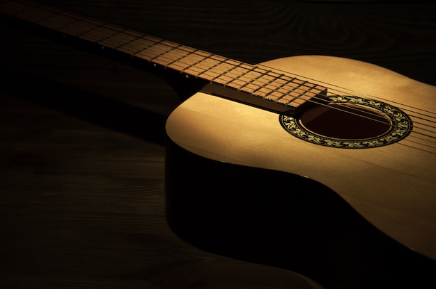 Ein lichtstrahl fällt auf eine akustikgitarre, die auf einem hölzernen strukturierten hintergrund liegt. Premium Fotos