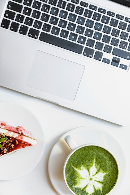 Eine draufsicht auf beeren-käsekuchen; matcha und laptop des grünen tees auf weißem schreibtisch Kostenlose Fotos
